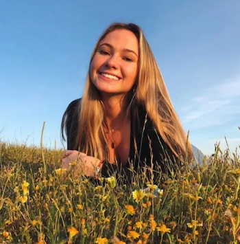 Una mujer joven sonríe acostada sobre la hierba entre flores amarillas bajo el cielo azul