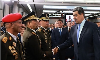 Nicolás Maduro con traje oscuro estrecha la mano a un militar uniformado junto a otros dos oficiales y varias personas en el fondo
