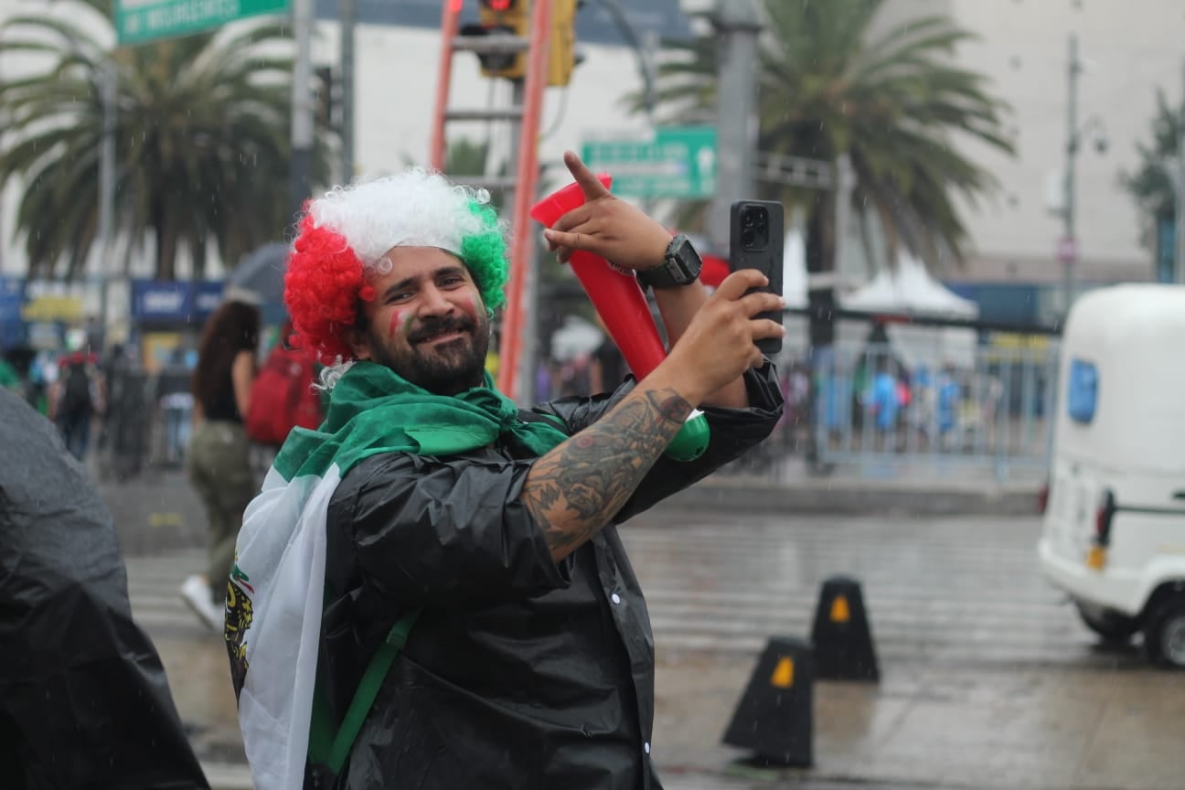 Un aficionado mexicano, vestido con los colores de su bandera y maquillaje facial, toma fotografías durante la despedida a la Selección Nacional en el Ángel de la Independencia, Ciudad de México. (@OVIALCDMX)