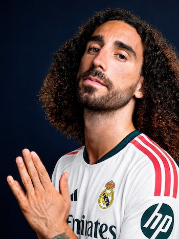 camiseta blanca de Real Madrid, logos Adidas, Emirates y HP, franjas rojas. Manos unidas en primer plano. Fondo azul oscuro