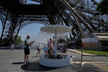 Gente se enfría con agua pulverizada cerca de la Torre Eiffel, en París, el 21 de junio de 2026, durante la ola de calor que atraviesa Francia. (Foto AP/Michel Euler)