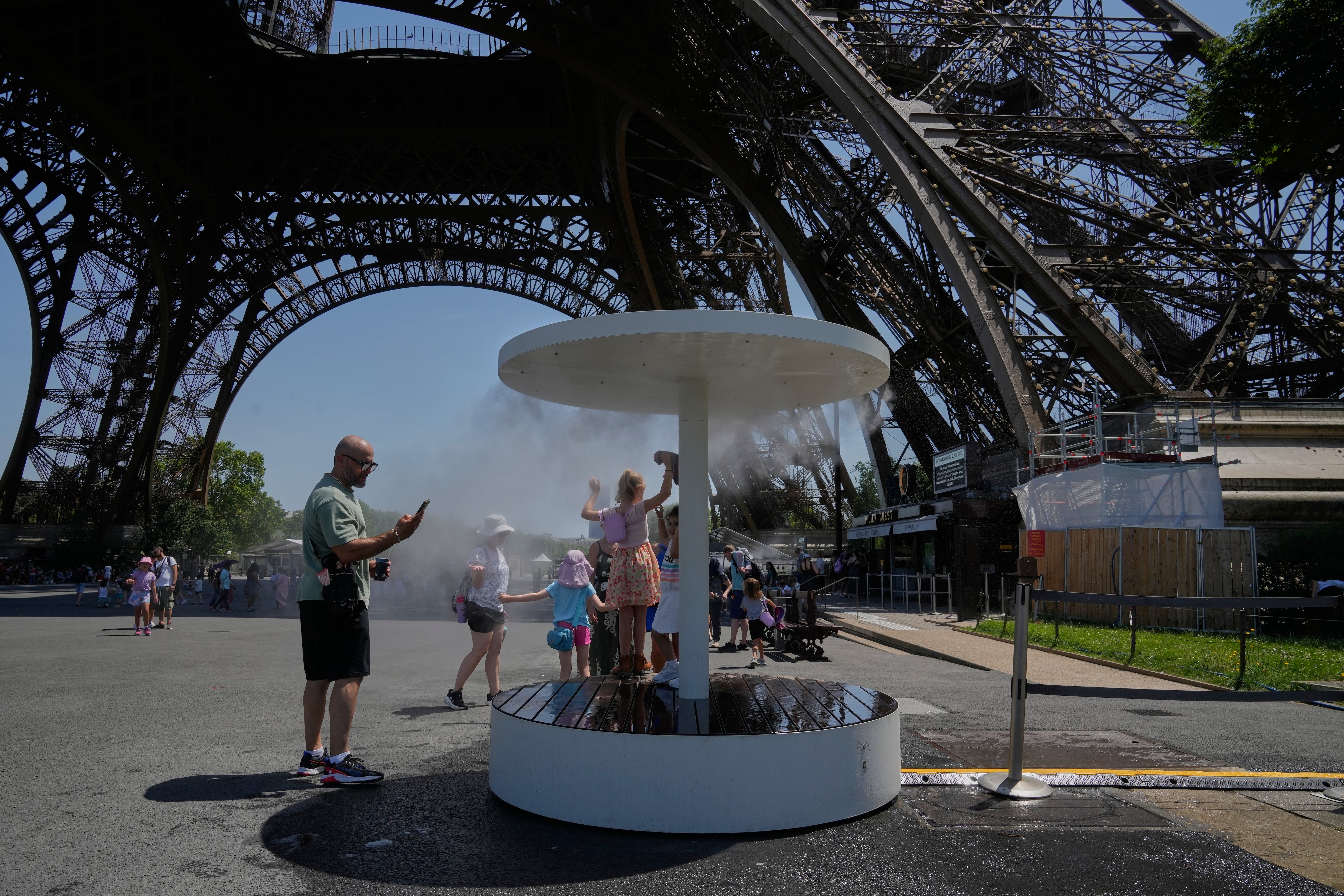 Gente se enfría con agua pulverizada cerca de la Torre Eiffel, en París, el 21 de junio de 2026, durante la ola de calor que atraviesa Francia. (Foto AP/Michel Euler)