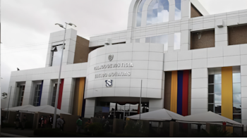 Edificio de varios pisos con fachada blanca, grandes ventanales y paneles decorativos rojos, azules y amarillos, con personas y toldos en la parte inferior