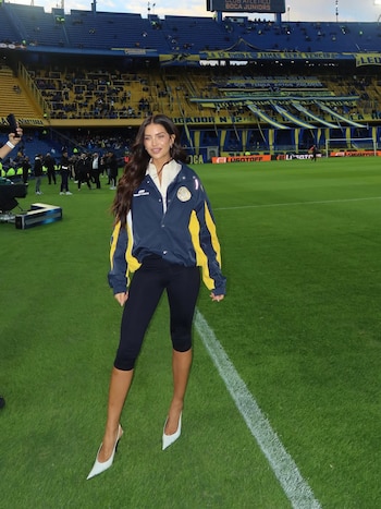 Zaira Nara sonríe en el campo de fútbol de La Bombonera, vestida con una chaqueta azul y amarilla, pantalones oscuros y tacones claros, con tribunas de fondo