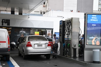 Un automóvil plateado en una estación de servicio YPF, con un empleado cargando combustible. Las bombas y un cartel digital de precios son visibles, y una tienda Full al fondo