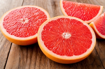 Dos mitades de pomelo rosado y dos gajos en forma de cuña sobre una mesa de madera.