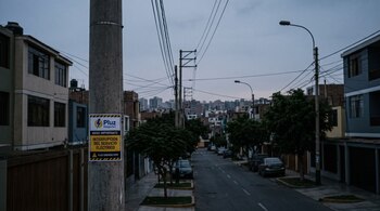 Aviso de interrupción del servicio eléctrico pegado en un poste de concreto sobre una calle residencial en penumbras.
