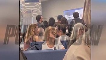 Imagen borrosa de un grupo de personas sentadas en una sala de espera. Se ven figuras de Sabrina Rojas y José Chatruc entre la gente, indistinguibles