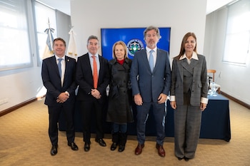 Cinco personas, tres hombres con traje y dos mujeres, posan delante de una pantalla con el logo del Ministerio de Justicia y dos banderas