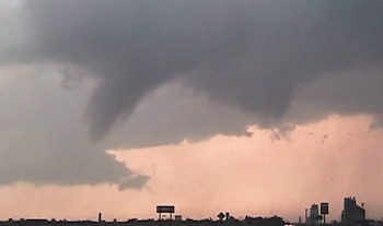 Cielo oscuro y turbulento con nubes de tormenta y una posible nube de embudo. Abajo, siluetas de edificios y un horizonte rojizo al atardecer