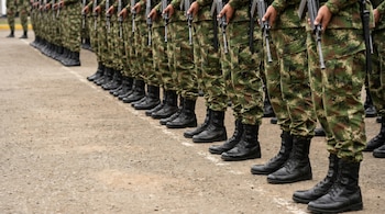 Plano cerrado de la mitad inferior del cuerpo de varios militares del Ejército de Colombia formados, vistiendo uniformes de camuflaje, botas negras y sosteniendo fusiles.