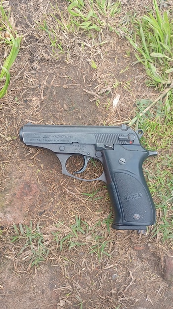 Una pistola negra con inscripciones de la marca Bersa colocada sobre un suelo de tierra y brotes de pasto