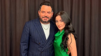 Un hombre con barba y chaqueta azul a rayas posa junto a una mujer de cabello oscuro con vestido verde.