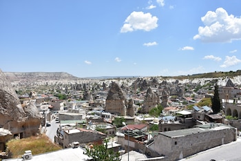 Amplia vista del pueblo de Goreme, con numerosas formaciones rocosas y casas de piedra incrustadas, bajo un cielo azul con nubes