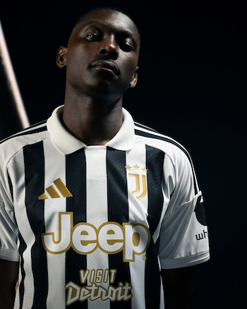Hombre de piel oscura con camiseta de fútbol de rayas blancas y negras, cuello blanco. Logotipos dorados de Adidas, Juventus, Jeep, Visit Detroit. Logotipo parcial en manga
