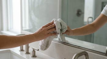 Una mano sostiene un calcetín blanco sobre la superficie de un espejo de baño junto a un lavabo con grifería metálica.