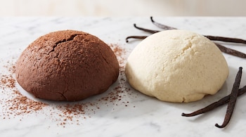 Dos masas para cubierta de concha, una de chocolate y otra de vainilla, sobre mármol. Incluye cacao en polvo y vainas de vainilla.