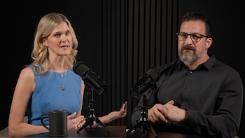 Dra. Natalie Crawford, mujer rubia con vestido azul, sentada frente a un micrófono junto a un hombre barbudo con camisa negra y gafas. Fondo oscuro acanalado