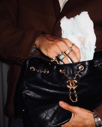 Mano con varios anillos que coloca un pañal desechable blanco dentro de un bolso de cuero negro con asas de cadena