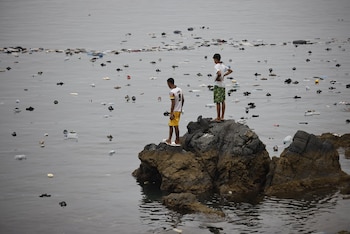 Dos jóvenes migrantes observan las chanclas y flotadores que flotan en el mar de la costa de Ceuta (Jesús Torres / Europa Press)