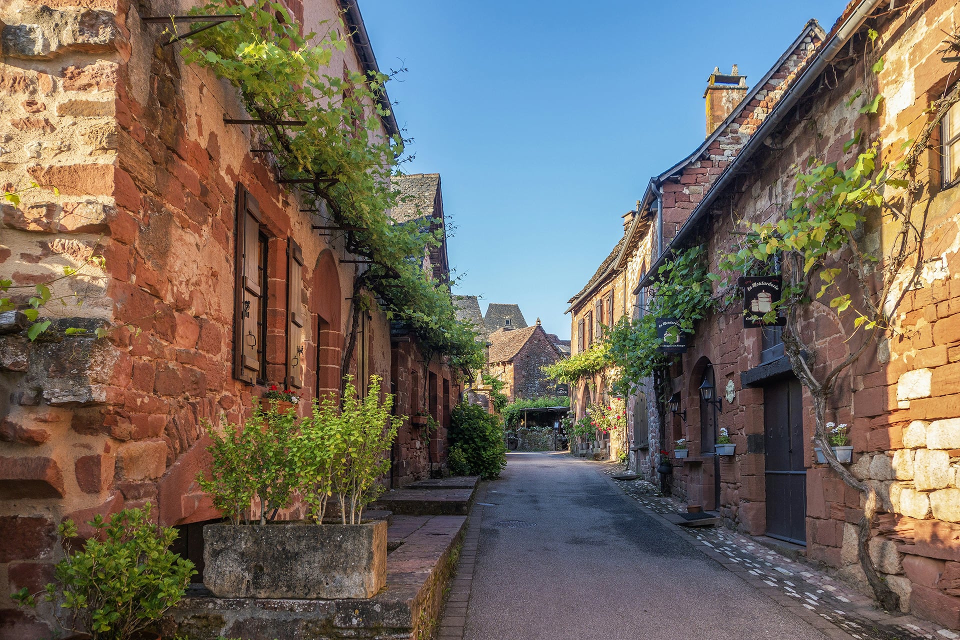 Una calle estrecha flanqueada por casas tradicionales de piedra roja se extiende en la localidad francesa de Collonges-la-Rouge. (Unsplash)