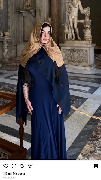 Karely Ruiz de pie en una sala del Vaticano, vestida con un velo dorado y un vestido azul oscuro, con estatuas clásicas al fondo