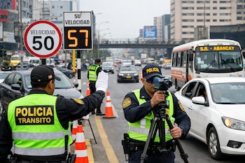 Dos policías peruanos de tránsito en uniforme y chalecos fluorescentes controlan el tráfico y la velocidad en una calle de Lima con un radar y señales viales.