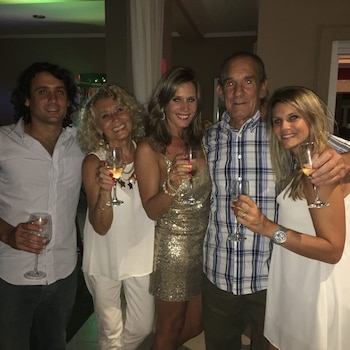 Cinco personas, tres mujeres y dos hombres, posan sonriendo y brindan con copas de vino o champán en un interior con luz ambiental