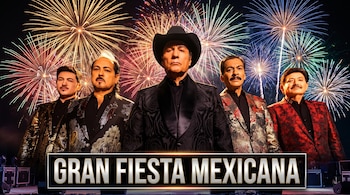 Cinco hombres vestidos con trajes de gala posan ante un espectáculo de fuegos artificiales con un letrero que dice Gran Fiesta Mexicana.