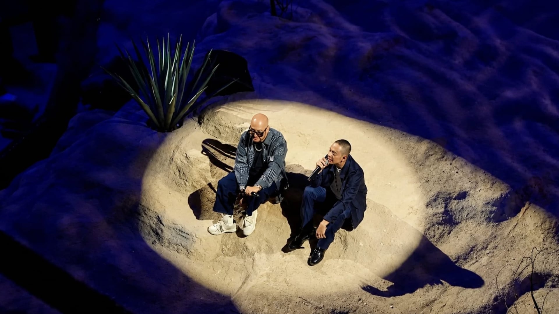 El cantante Natanael Cano interpreta un tema junto a un invitado sobre una escenografía iluminada por un foco durante su concierto en el Estadio GNP Seguros. (X)