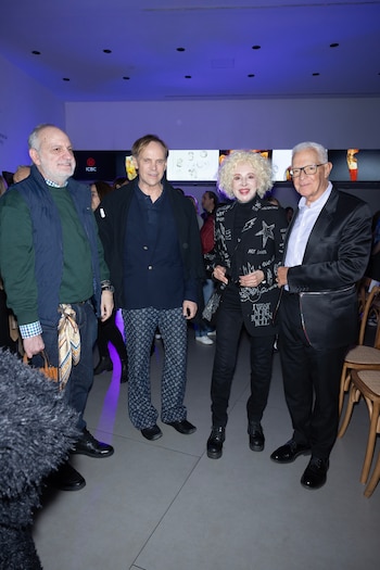 Tres hombres y una mujer posan de pie en un recinto interior con iluminación azul y pantallas de fondo