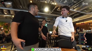 Dos hombres en un restaurante. El de la izquierda, con camiseta negra, de perfil. El de la derecha, con camiseta blanca y gafas oscuras, gesticula acaloradamente