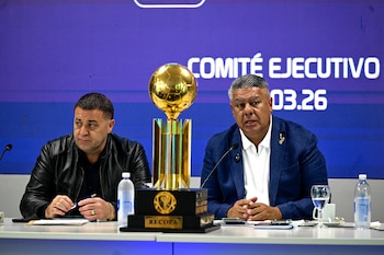 Claudio Tapia y Pablo Toviggino, junto a un trofeo dorado de la Recopa, están sentados en una mesa con micrófonos, con una pantalla azul de fondo