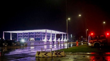 Edificio iluminado del Supremo Tribunal Federal de noche, con camión de bomberos, vehículos policiales y asfalto mojado bajo la lluvia