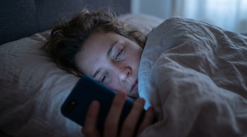 Primer plano del rostro de una mujer acostada en la cama, que mira un teléfono móvil que sostiene con su mano y emite luz sobre su cara.
