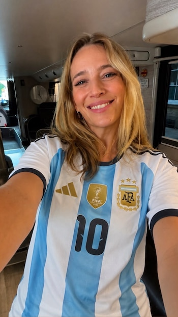 Luisana Lopilato sonríe, cabello rubio, viste camiseta de fútbol con rayas celestes y blancas, número 10, escudo AFA y parche FIFA 2022