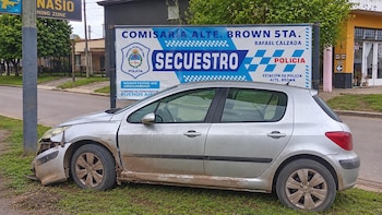 Automóvil gris con el frente dañado estacionado sobre el pasto junto a un poste y un cartel policial