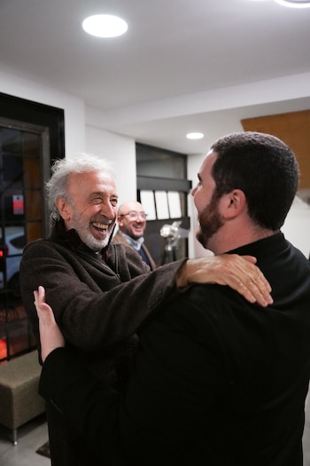 Eduardo Blanco, hombre de cabello y barba gris, ríe mientras abraza por el cuello a Gastón Cocchiarale, de espalda con barba oscura