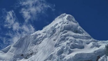 Montanhas nevadas de Nevado Tocllaraju sob um céu azul brilhante com nuvens dispersas, mostrando geleiras e rochas cobertas de gelo