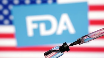 Uma seringa extrai um líquido transparente de um pequeno frasco, com um rótulo fraco da FDA e uma bandeira americana no verso.