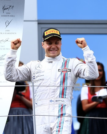 Valtteri Bottas, piloto de Fórmula 1, en un traje de carreras blanco con rayas rojas y azules y gorra Pirelli, sonríe con los puños levantados en el podio