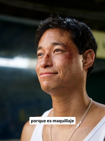 Hombre sonriendo con maquillaje que simula moretones y una herida en nariz y mejilla. Lleva camiseta blanca y cadena plateada. Texto: porque es maquillaje