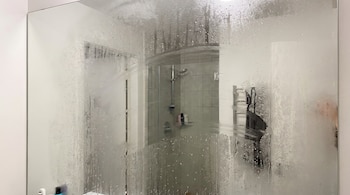 Un espejo de baño grande cubierto casi por completo de vapor, con gotas de agua y rayas limpias que muestran el reflejo de la ducha.