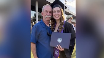 Un hombre con bigote en camisa azul abraza a una mujer joven con toga y birrete de graduación, ambos sonriendo y ella sosteniendo un diploma