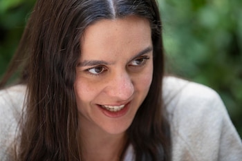 Primer plano de Valeria Castro, mujer joven de pelo largo y oscuro, con sonrisa sutil y mirada hacia la derecha, sobre fondo verde difuminado