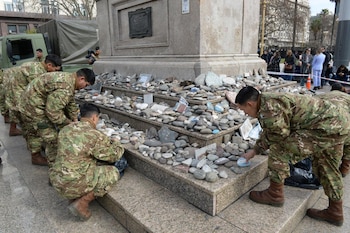 Grupo de personas con uniforme militar camuflado ordena piedras lisas en la base escalonada de un monumento al aire libre