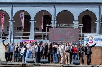 Un grupo de personas sobre un escenario al aire libre frente a una pantalla del Festival Nacional de Folklore de Cosquín