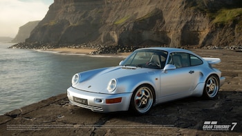 Un Porsche 911 Turbo S plateado, de la generación 993, estacionado sobre un muelle de piedra junto a un mar tranquilo y acantilados rocosos