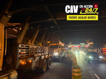 Camiones y maquinaria de trabajo estacionados en el carril de una avenida iluminada junto a un puente por la noche