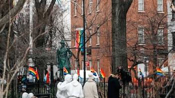 Vista del Monumento Nacional Stonewall con estatuas, banderas arcoíris, árboles desnudos y un edificio de ladrillo al fondo en un día nublado